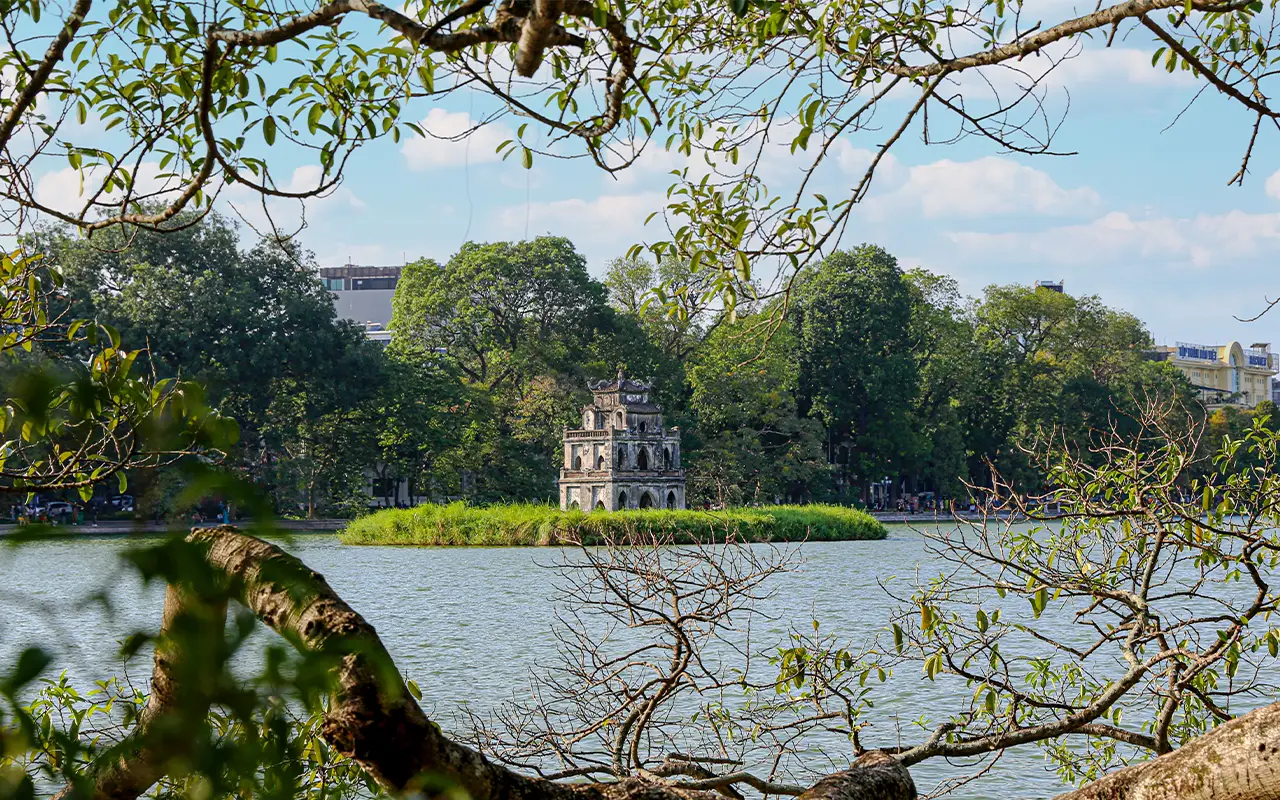 Turtle Tower on Hoan Kiem Lake in Hanoi, Vietnam, framed by green tree branches