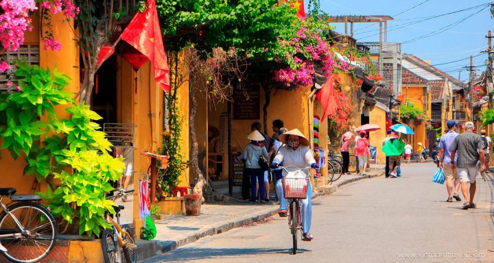 Locals and tourists strolling down a charming street in Hoi An on a sunny day.