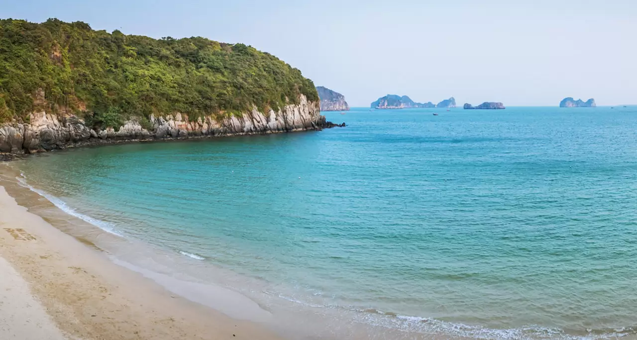 A scenic view of a white sand beach, a blue sea and green mountains at Cat Ba Island