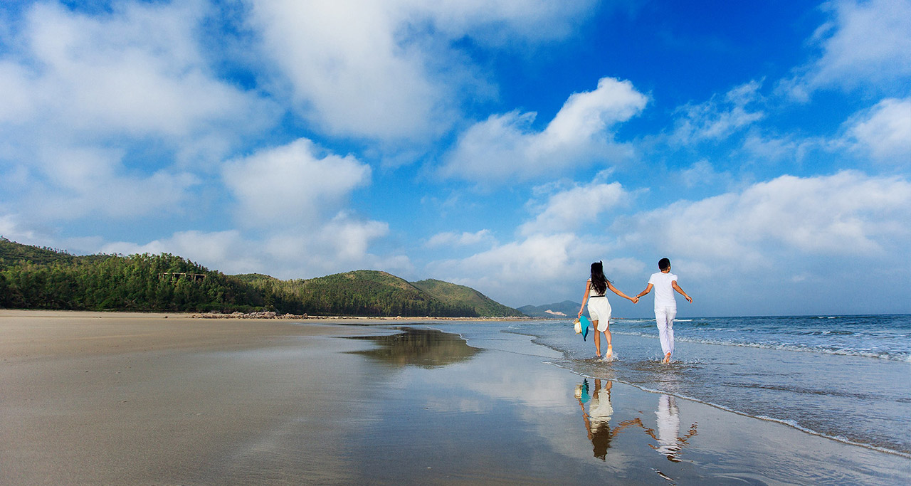 A happy couple in white outfits walking on the beach at Quan Lan Beach