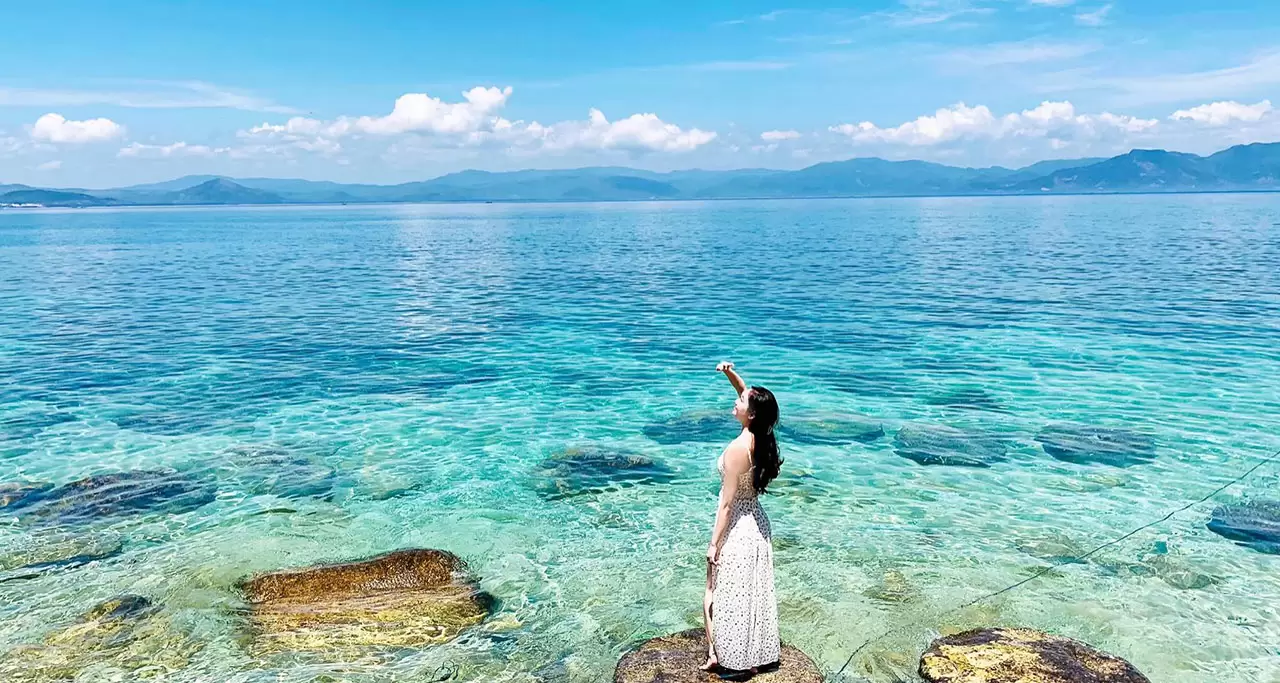 Photo of a girl in a beautiful dress standing on a rock with clear and blue sea water in Cu Lao Xanh, Quy Nhon
