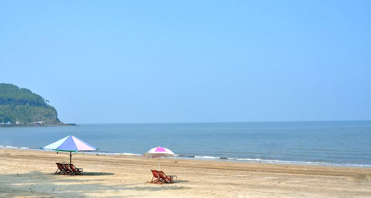 A beach resort with umbrellas, chairs, blue water and a hill at Do Son Beach, Hai Phong