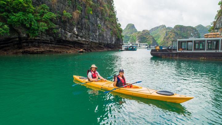 Kayaking through the emerald waters of Halong Bay in July, with limestone formations in the background.