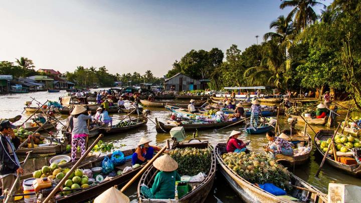 A colorful floating market on the Mekong River in July, filled with boats overflowing with fresh produce.