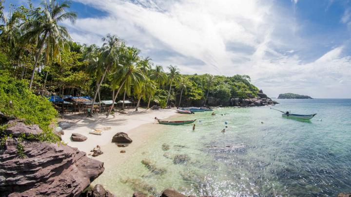 Relaxing beach scene on Phu Quoc Island in July with turquoise water, palm trees, and a partly cloudy sky.