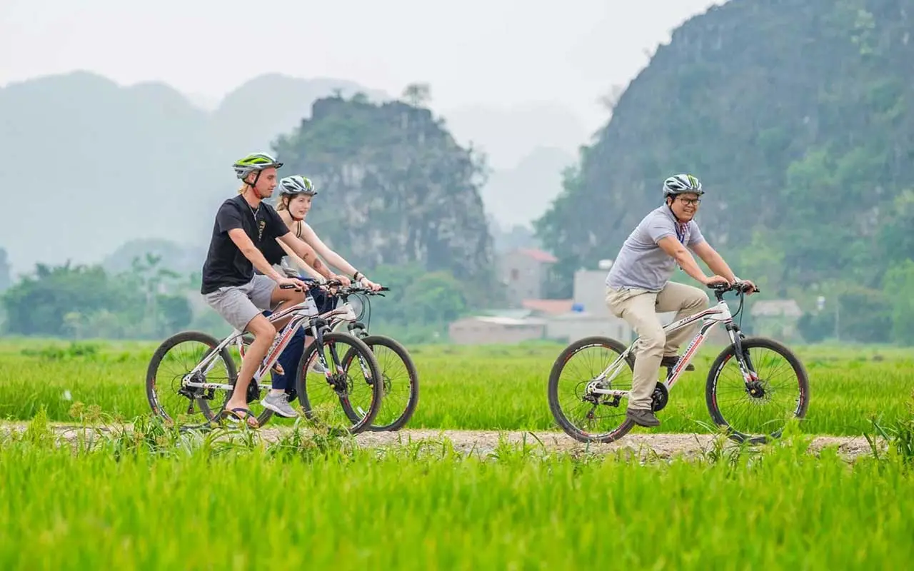 Tourists riding a bicycle along a rural road surrounded by rice fields and mountains in Ninh Binh
