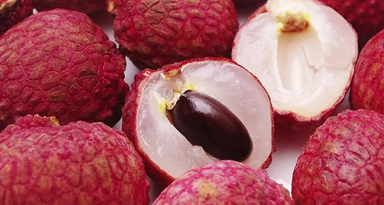 Close-up image of few fruits with 1 peeled fruit visible pulp and lychee seeds