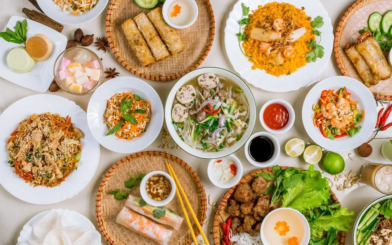 Flat-lay spread of traditional Vietnamese dishes including pho, spring rolls, and fresh herbs