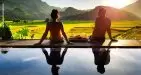 A couple seated on the edge of a swimming pool, surrounded by mountains and greenery, enjoying the tranquil scenery at Mai Chau Ecolodge.